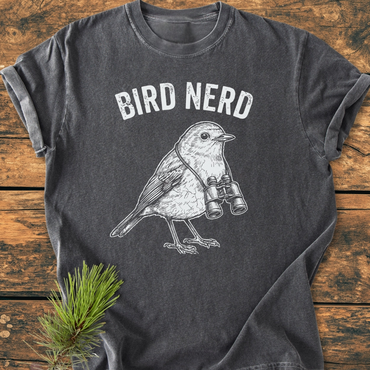 Bird Nerd - Vintage Wash Tee on wooden surface, features a white songbird with binoculars illustration and BIRD NERD slogan. Made from soft, garment-dyed, 100% ring-spun cotton for comfort and durability.