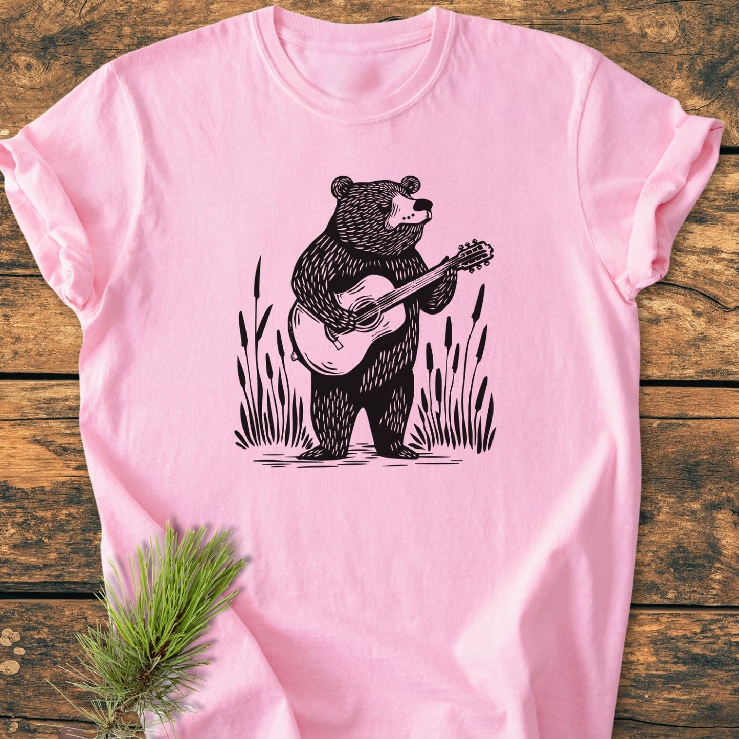 Bear Playing Guitar - Vintage Wash Tee features a stylized bear with a guitar graphic on a light-pink, soft-washed T-shirt, laid flat with a pine sprig accentuating its relaxed fit.