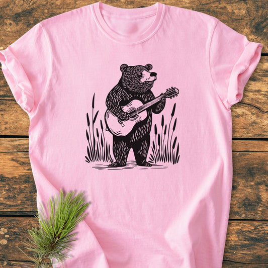 Bear Playing Guitar - Vintage Wash Tee features a stylized bear with a guitar graphic on a light-pink, soft-washed T-shirt, laid flat with a pine sprig accentuating its relaxed fit.
