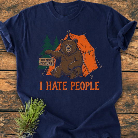 Navy-blue I Hate People - Vintage Wash Tee with a cartoon grumpy bear holding a DO NOT DISTURB sign, sitting by an orange tent, laid on a wooden surface.