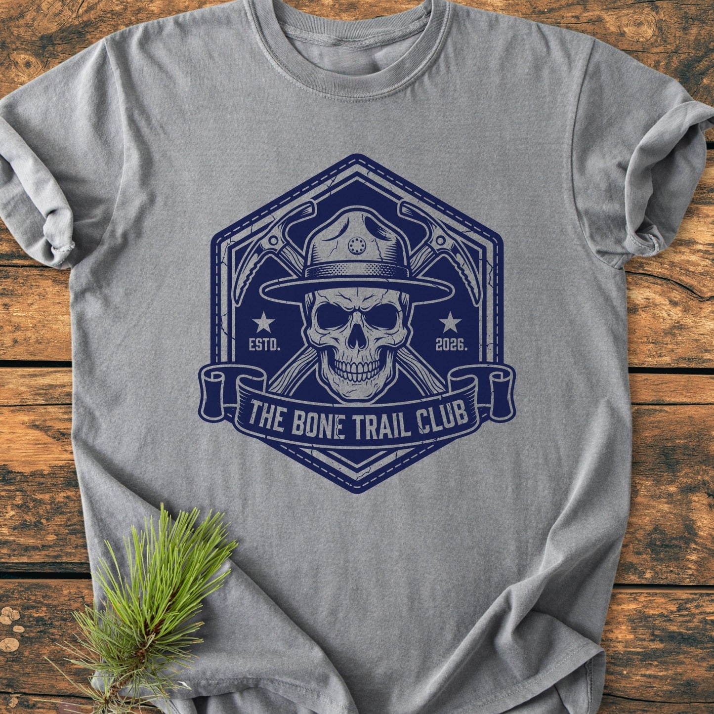 The Bone Trail Club - Vintage Wash Tee features a skull with a ranger hat, crossed ice-axes, and THE BONE TRAIL CLUB banner, on a heather-gray garment, offering a rugged outdoor aesthetic.