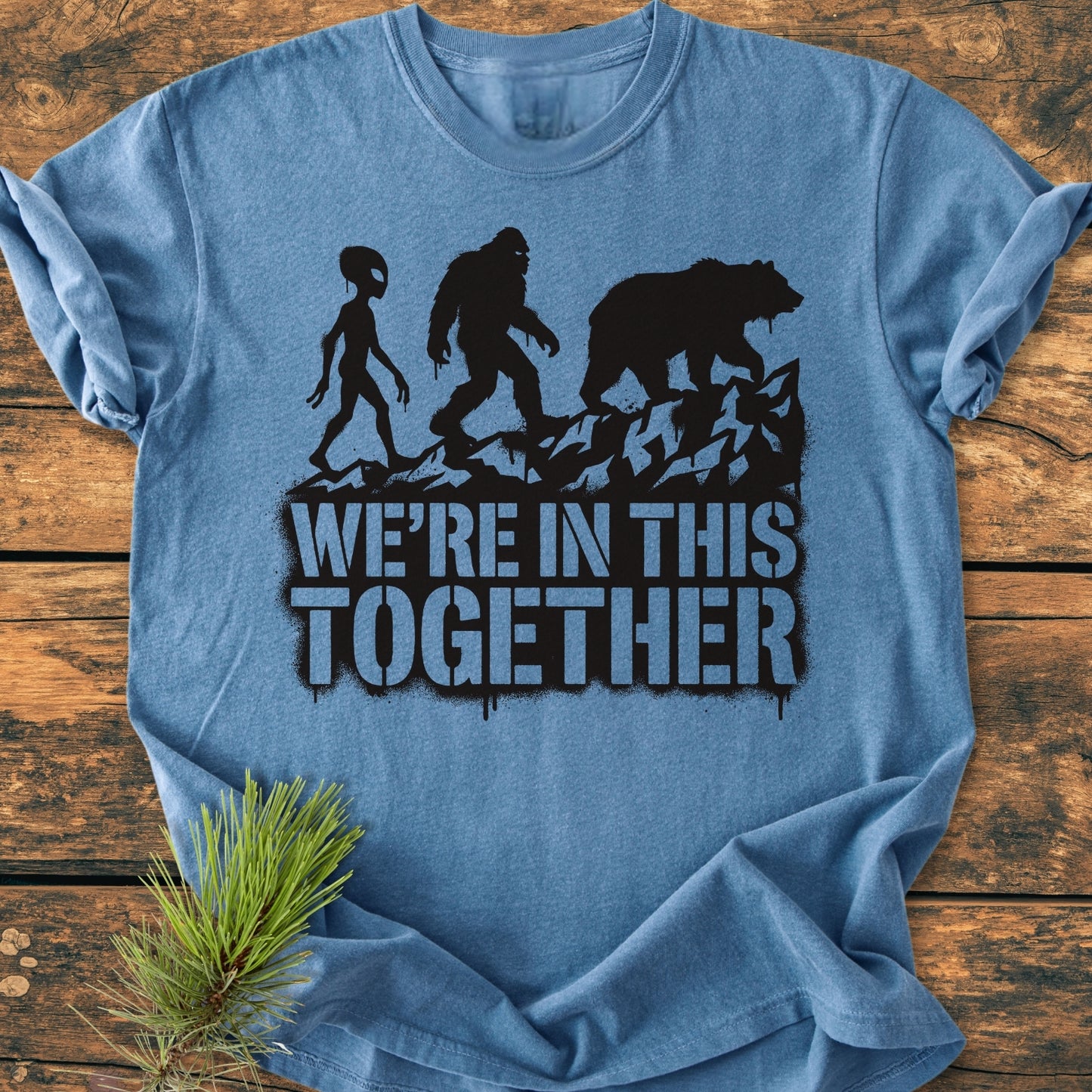 In This Together - Vintage Wash Tee, featuring silhouettes of an alien, Bigfoot, and a bear walking on a ridge, with 'WE’RE IN THIS TOGETHER' text on a soft, relaxed-fit blue garment.