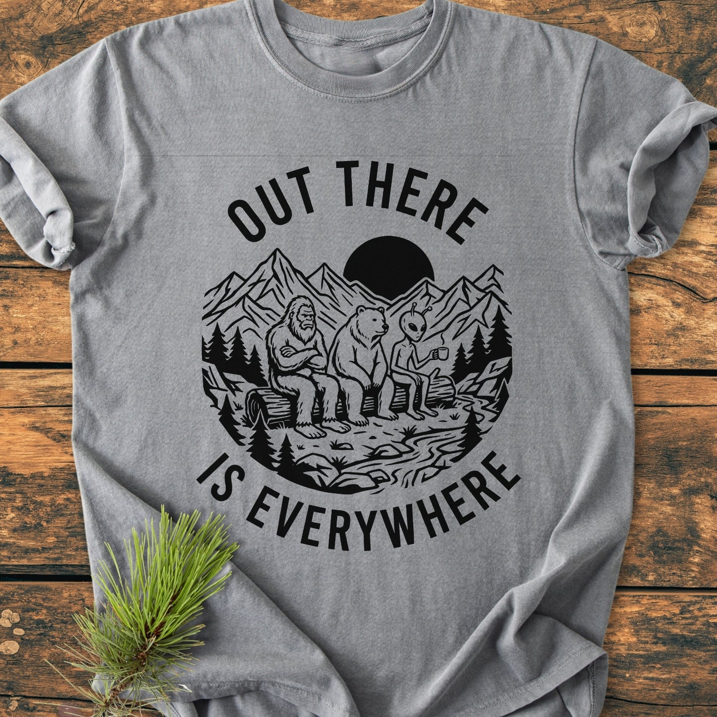 Out There Is Everywhere - Vintage Wash Tee featuring a wilderness scene with Bigfoot, bear, and alien on a log. Heather-gray, soft-washed cotton, relaxed fit, and durable with double-needle stitching.