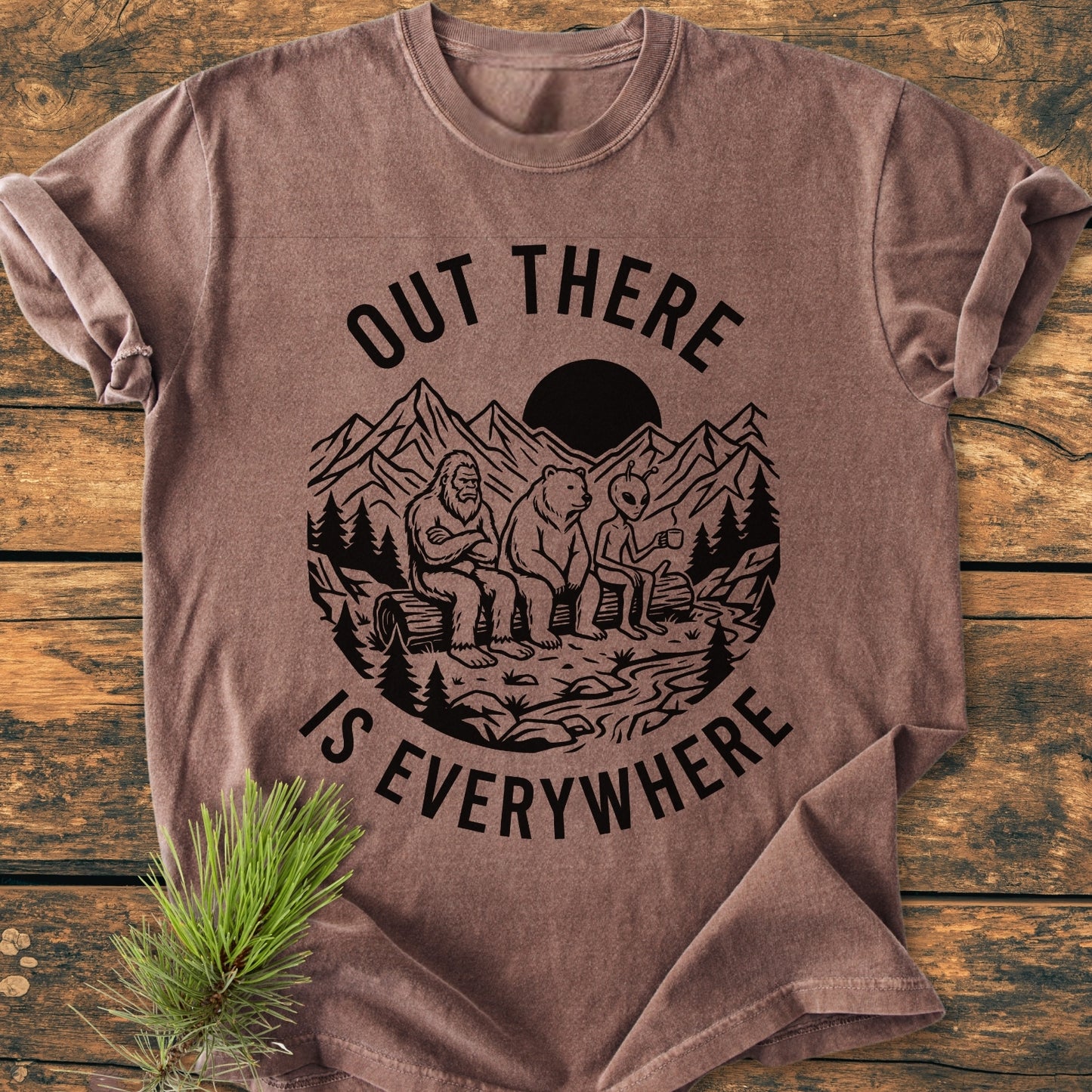 Out There Is Everywhere - Vintage Wash Tee featuring a circular graphic of Bigfoot, bear, and alien by a stream, surrounded by OUT THERE IS EVERYWHERE text, styled with a pine branch.