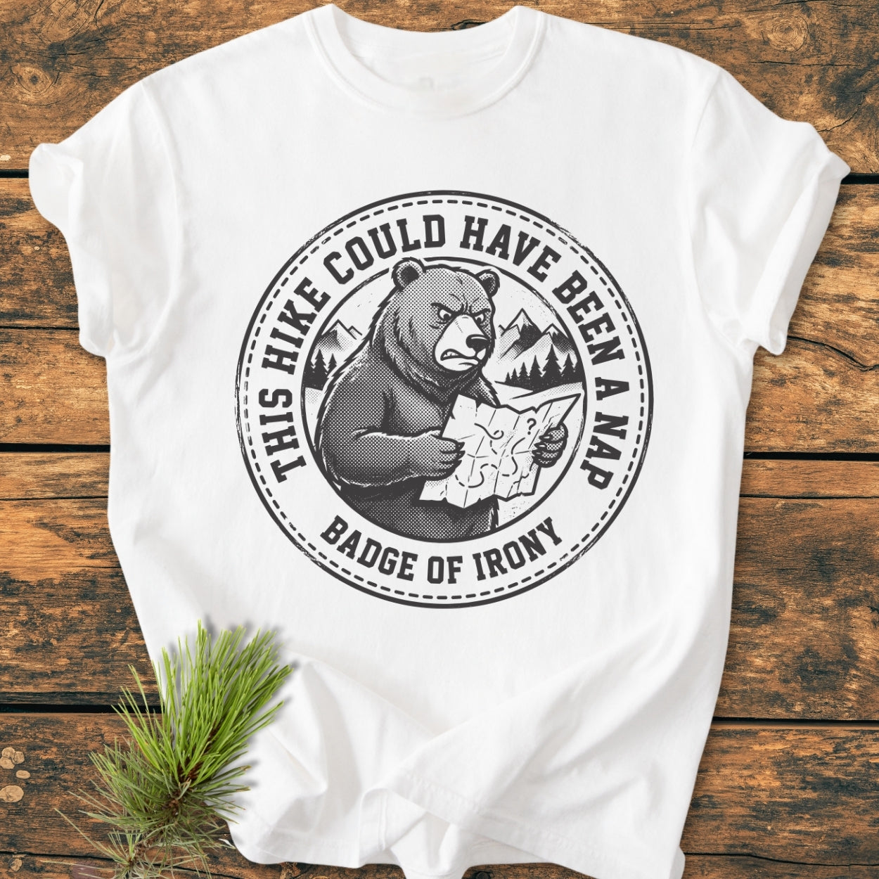 Could Have Been A Nap - Vintage Wash Tee featuring a black circular graphic with a bear, mountains, and trees. Text reads “THIS HIKE COULD HAVE BEEN A NAP.” Laid on a wooden surface with a pine branch.