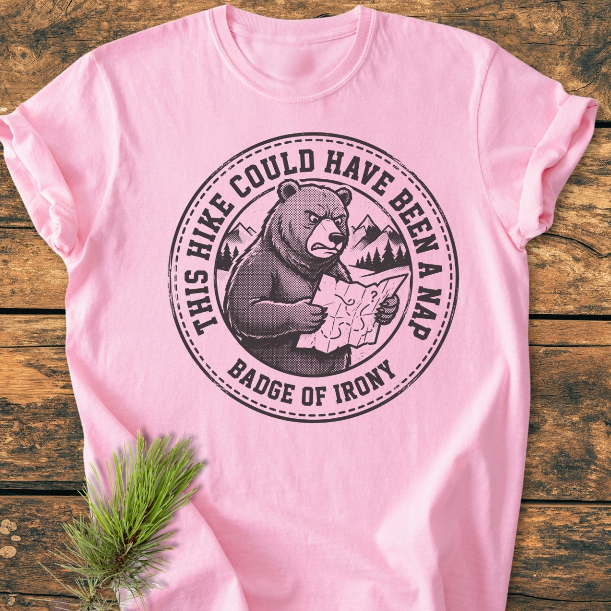 The Could Have Been A Nap - Vintage Wash Tee features a cartoon bear graphic with humorous text, laid on a wooden surface with pine needles, highlighting its relaxed fit and durable design.