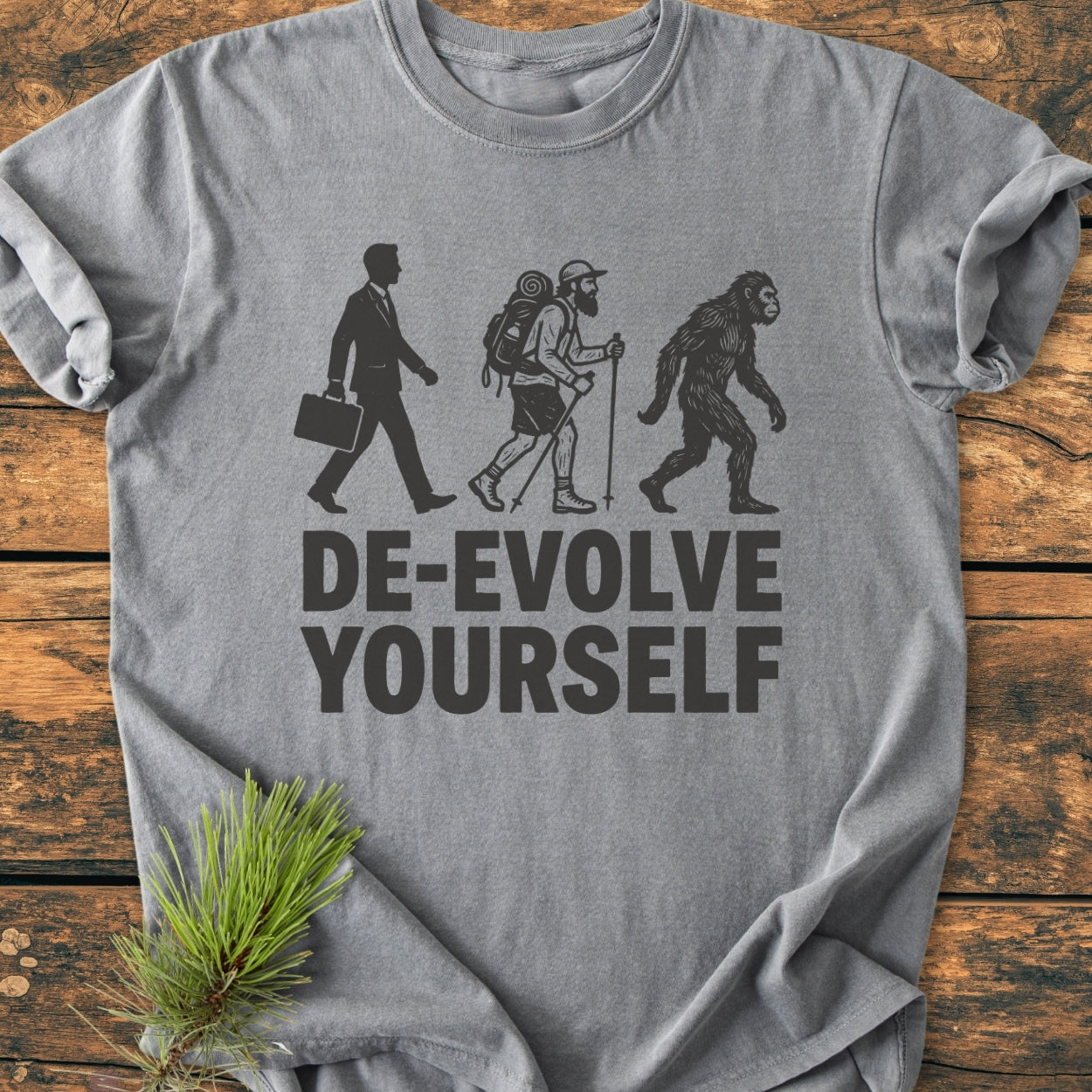 De-Evolve Yourself - Vintage Wash Tee features black silhouettes of a businessman, hiker, and ape with DE-EVOLVE YOURSELF. slogan on a grey, soft-washed, relaxed-fit t-shirt.