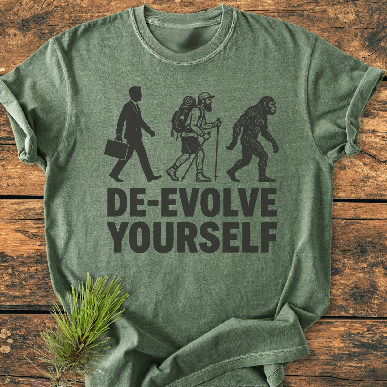 De-Evolve Yourself - Vintage Wash Tee: A green heather-style T-shirt with reverse-evolution silhouettes and slogan, laid on wood. Made from 100% ring-spun cotton, it offers a relaxed fit and durable design.