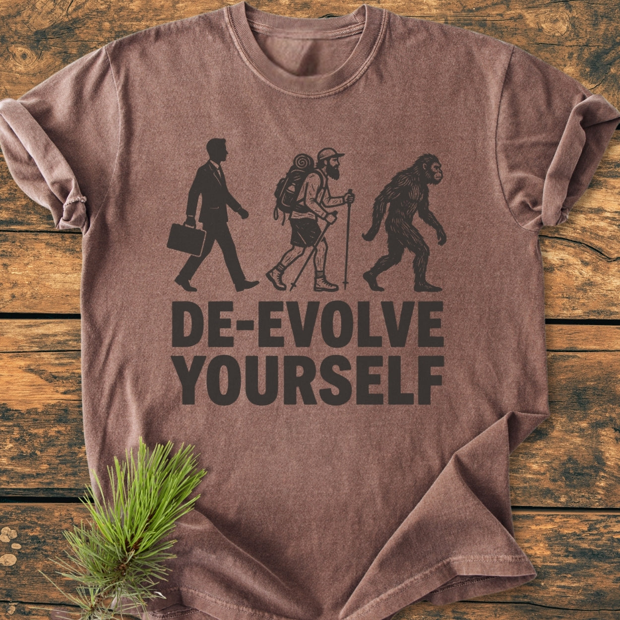 De-Evolve Yourself - Vintage Wash Tee features a reverse evolution print on a brown short-sleeve, laid flat on wood, highlighting its cozy, relaxed fit with durable, garment-dyed 100% ring-spun cotton.