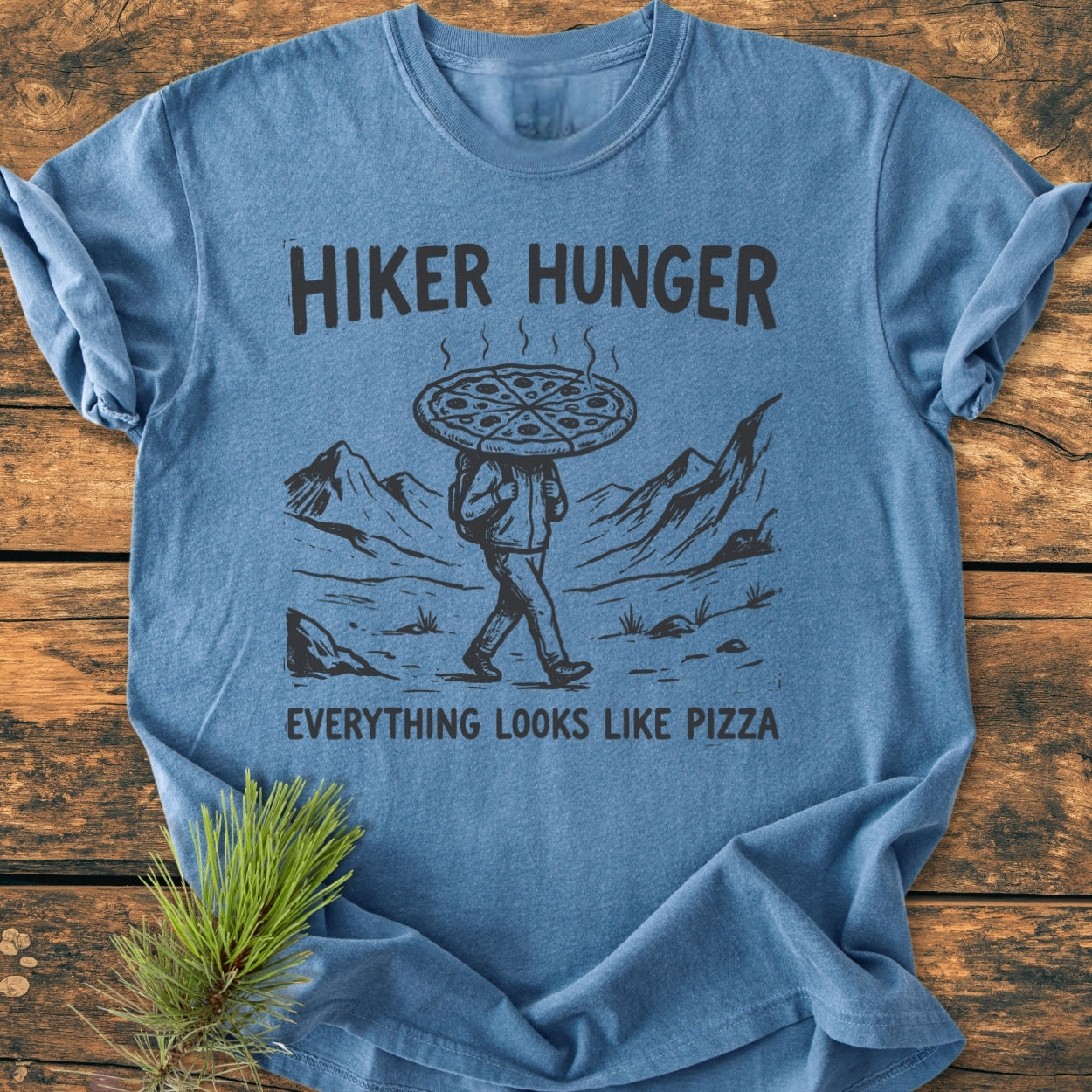 Hiker Hunger - Vintage Wash Tee features a unique graphic of a hiker with a pizza head on a heather-blue T-shirt, complemented by the slogan EVERYTHING LOOKS LIKE PIZZA, and adorned with a pine sprig.