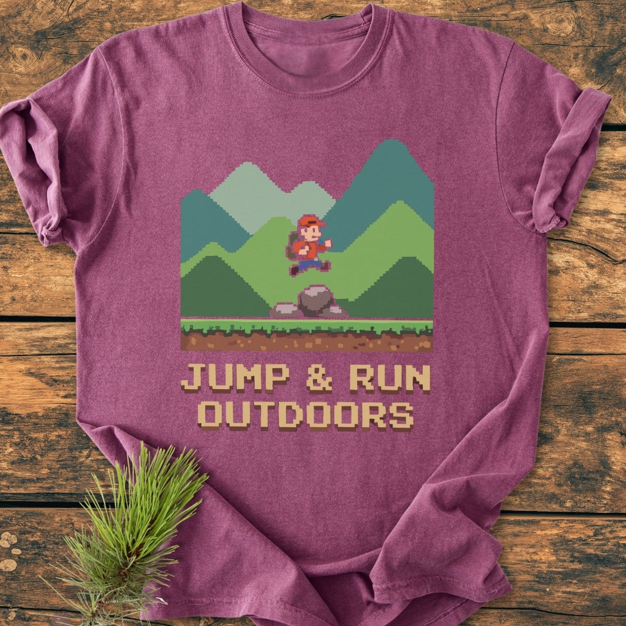 Jump And Run Outdoors - Vintage Wash Tee: A maroon-purple T-shirt with 8-bit graphics of a backpacker jumping over a rock, set against green mountains, with JUMP & RUN OUTDOORS text in pixel font.