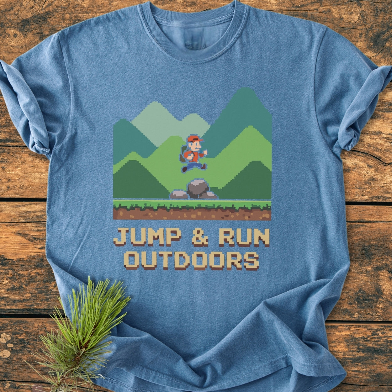 Jump And Run Outdoors - Vintage Wash Tee features an 8-bit hiker scene on a heather-blue T-shirt, laid flat with a pine twig accent, showcasing its cozy, garment-dyed fabric and relaxed fit.