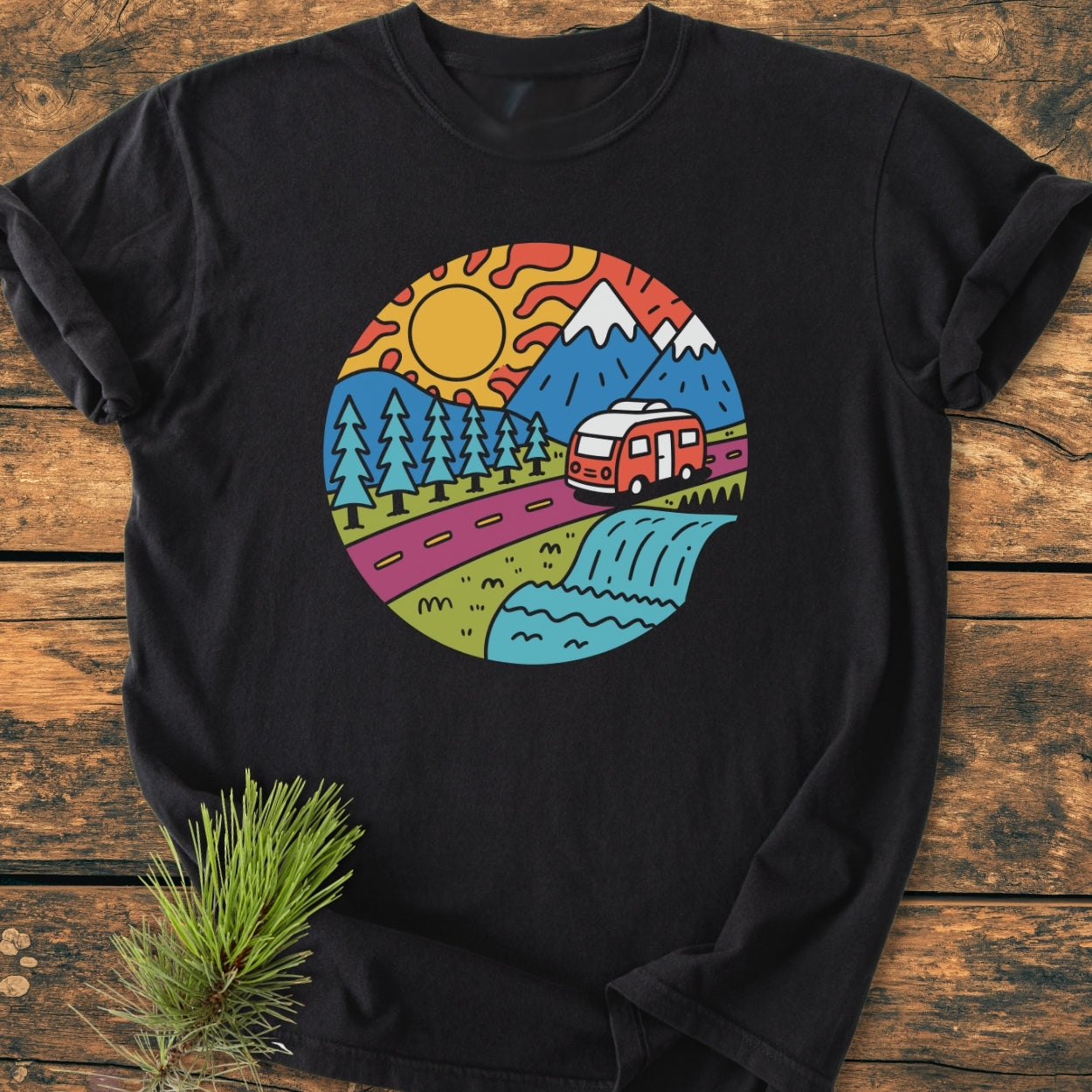 Scenic Route - Vintage Wash Tee featuring a cheerful, cartoon-style graphic of a nature and road-trip scene with mountains, trees, a sun, and a camper van on a black, garment-dyed T-shirt.