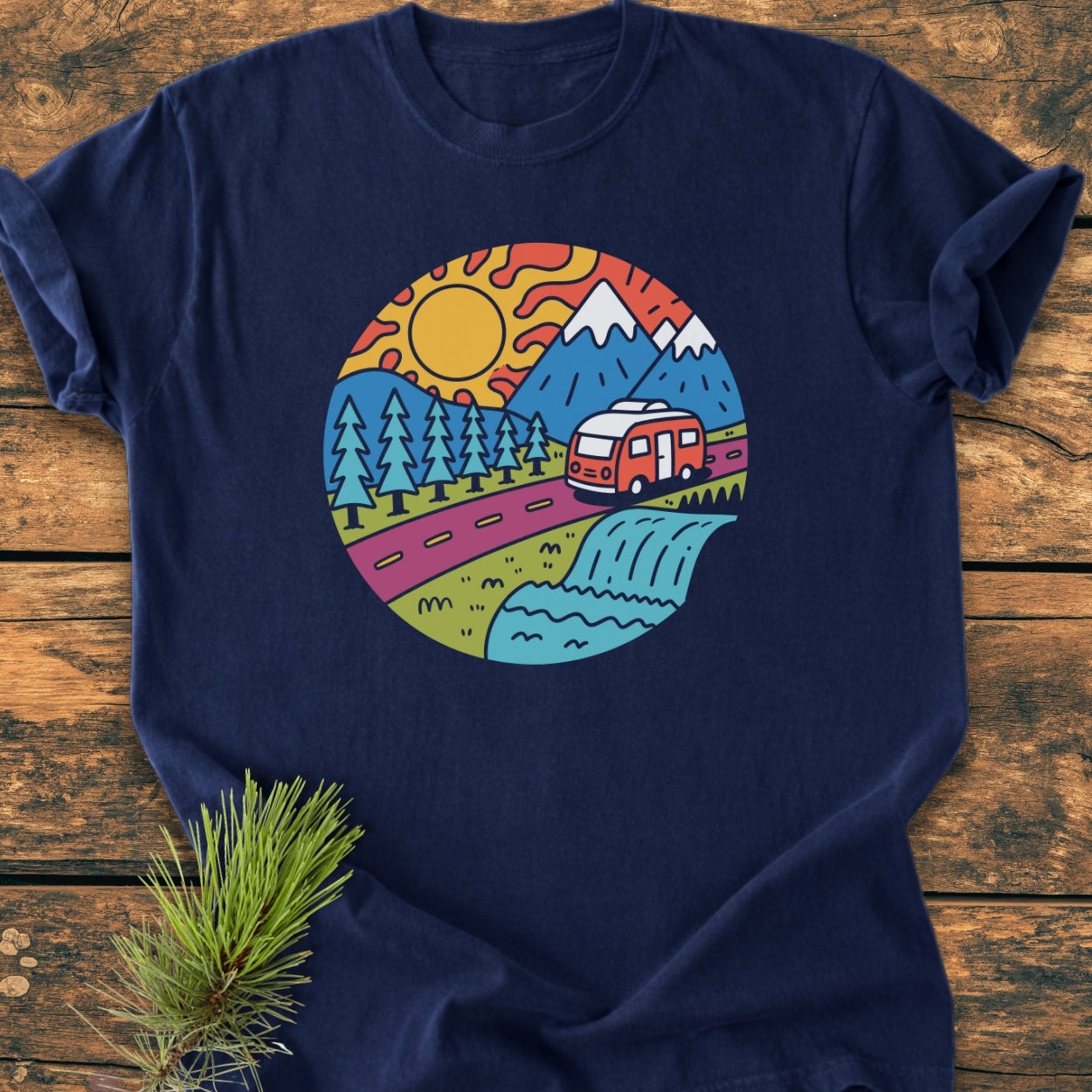 Scenic Route - Vintage Wash Tee featuring a vibrant outdoor scene with mountains, pine trees, and a camper van, laid on a wooden surface. Cozy, relaxed fit in garment-dyed, soft-washed cotton.