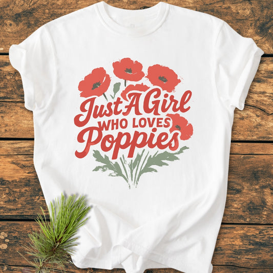 The Just A Girl Who Loves Poppies - Vintage Wash Tee features red poppies and green stems on a white background, laid on wood, complemented by a pine sprig.