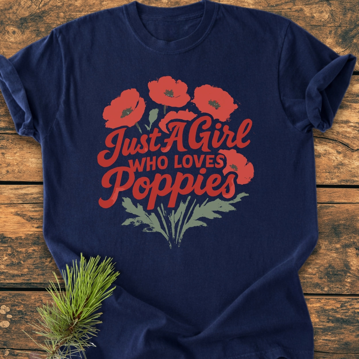 Just A Girl Who Loves Poppies - Vintage Wash Tee: Navy-blue tee featuring red poppy print and text, laid on wood, with a pine sprig under the hem. Cozy, relaxed fit, 100% cotton.