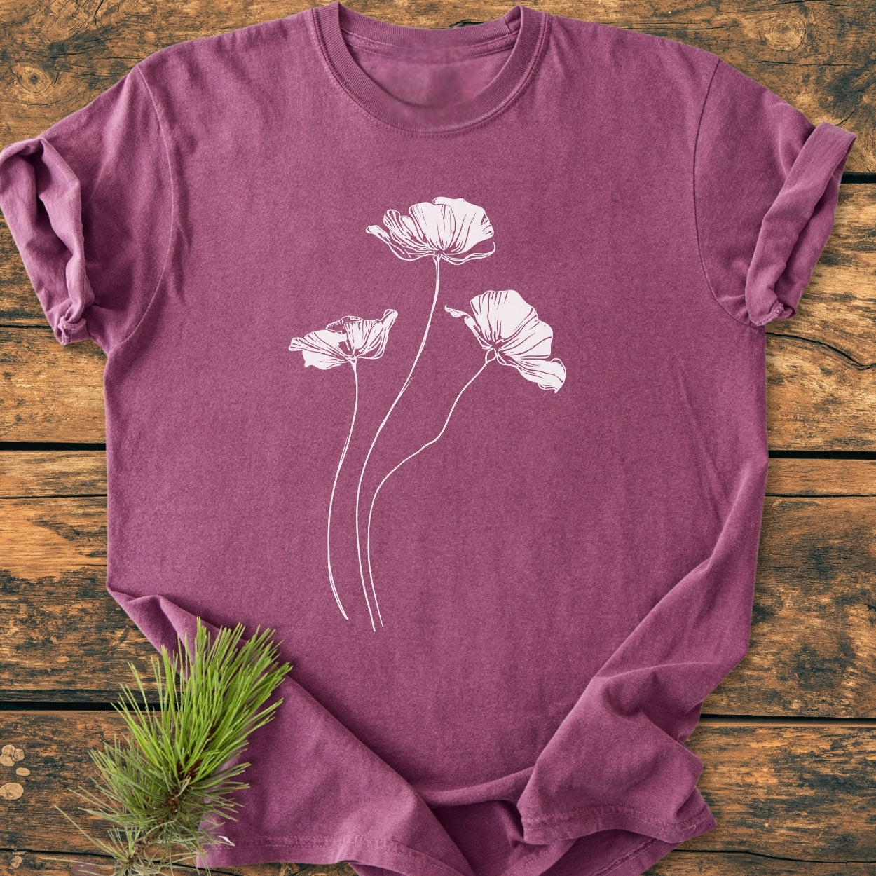 Delicate Poppies - Vintage Wash Tee: A heather-purple crew-neck T-shirt with white poppy line-drawings, arranged on rustic wood with a pine sprig accent, highlighting its relaxed fit and garment-dyed texture.