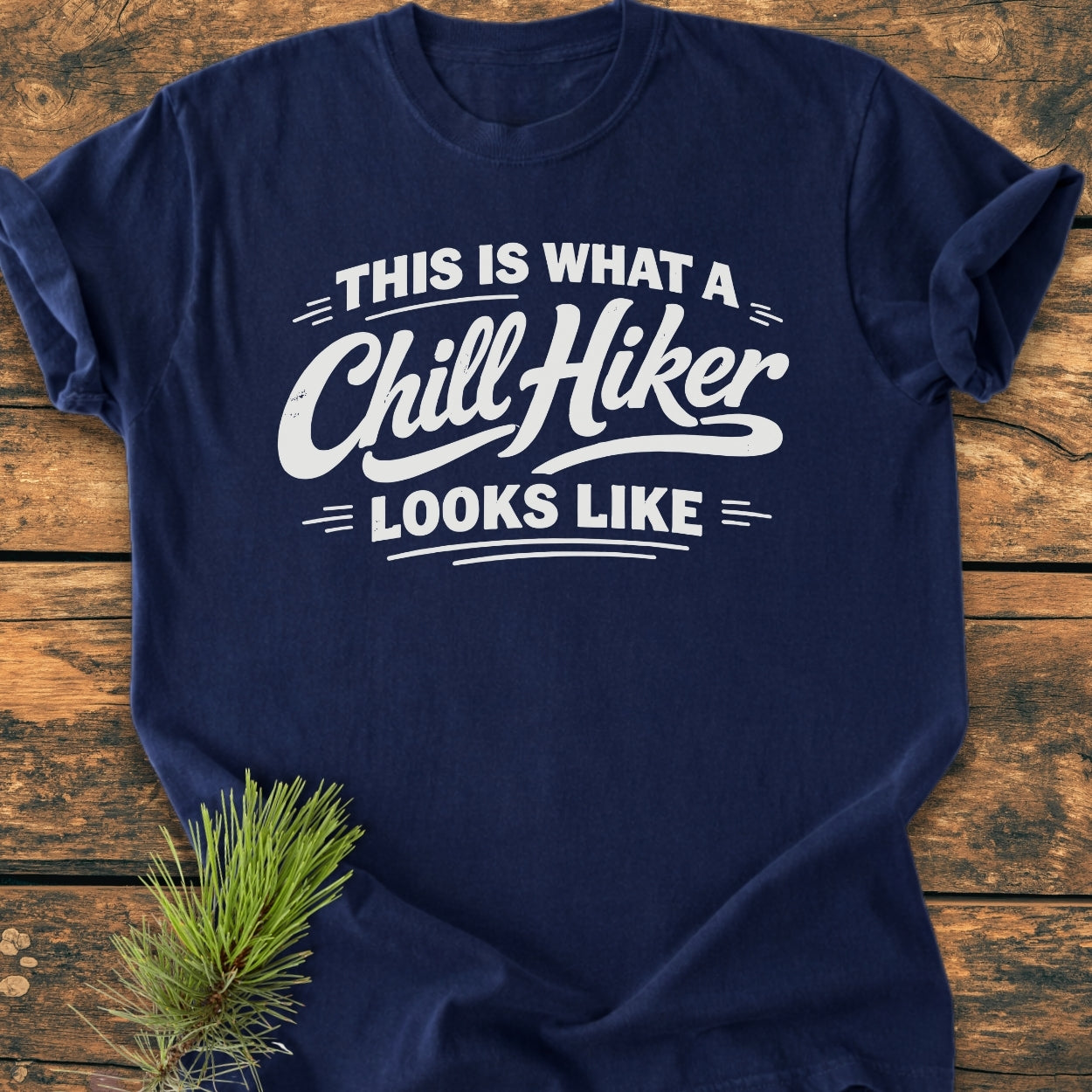 Navy-blue Chill Hiker - Vintage Wash Tee on wooden surface, featuring bold white text. Crafted with 100% ring-spun cotton, it offers a soft, relaxed fit. Pine branch accent in the corner.