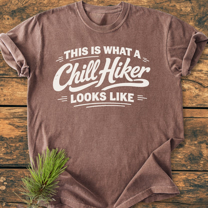 Chill Hiker - Vintage Wash Tee displayed on wood, featuring white text. Sleeves are rolled up; a pine sprig decorates the corner, showcasing the relaxed fit and cozy fabric.