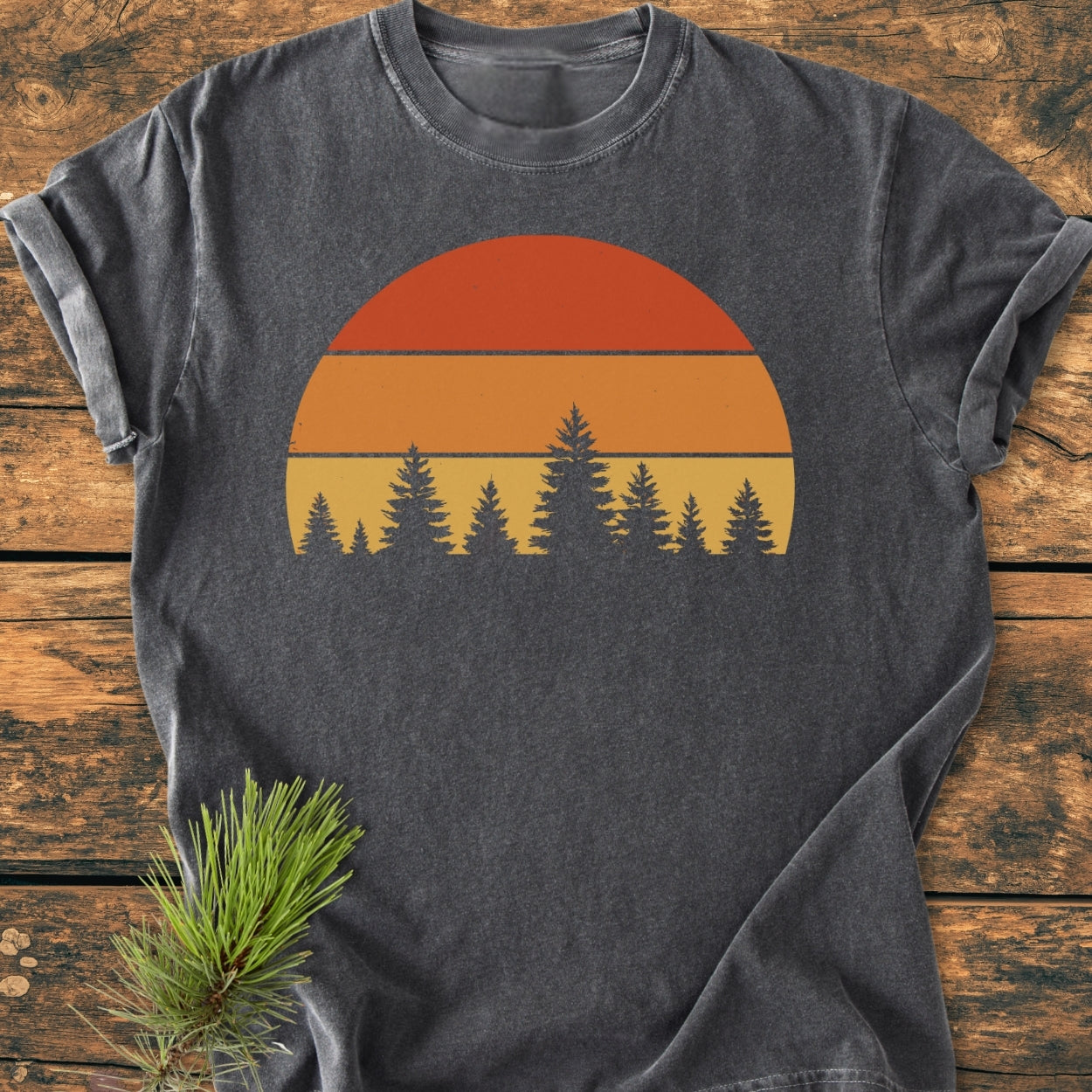 Forest Sunset - Vintage Wash Tee displayed on wood, features a retro half-sun graphic with pine silhouettes. Made from soft, garment-dyed 100% ring-spun cotton, offering a relaxed fit and durable stitching.