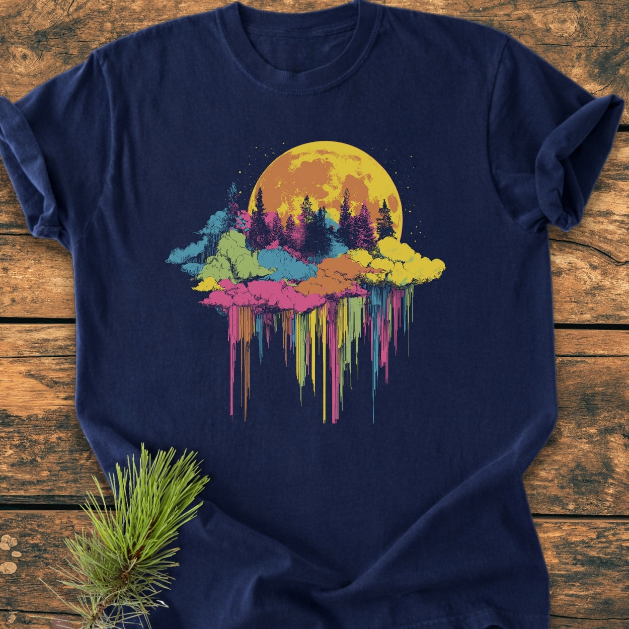 Moonlight Meltdown - Vintage Wash Tee features a vibrant moonrise graphic over evergreen silhouettes, laid on a wooden surface with a pine sprig, showcasing its relaxed fit and durable double-needle stitching.