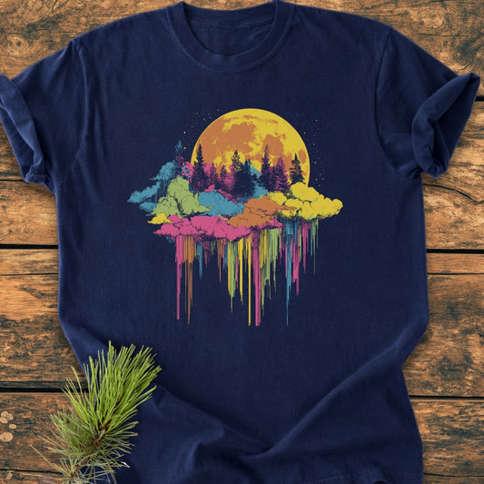 Moonlight Meltdown - Vintage Wash Tee features a vibrant moonrise graphic over evergreen silhouettes, laid on a wooden surface with a pine sprig, showcasing its relaxed fit and durable double-needle stitching.