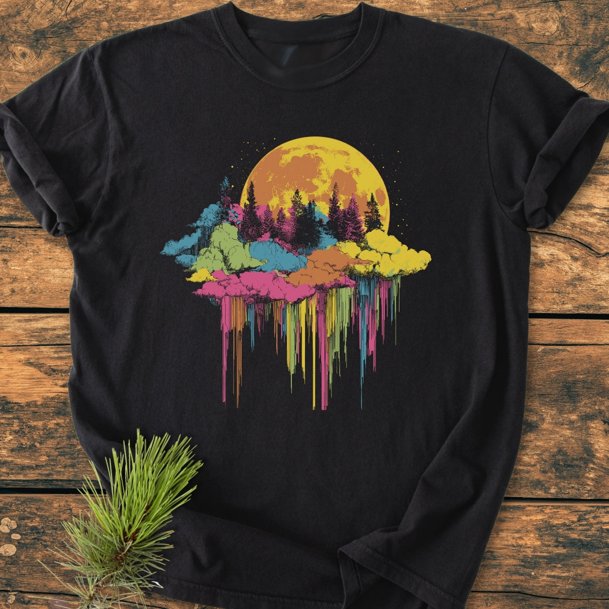 Moonlight Meltdown - Vintage Wash Tee on rustic wood, features a surreal glowing moon above multicolored clouds and pine tree silhouettes, with a dreamlike dripping paint effect.