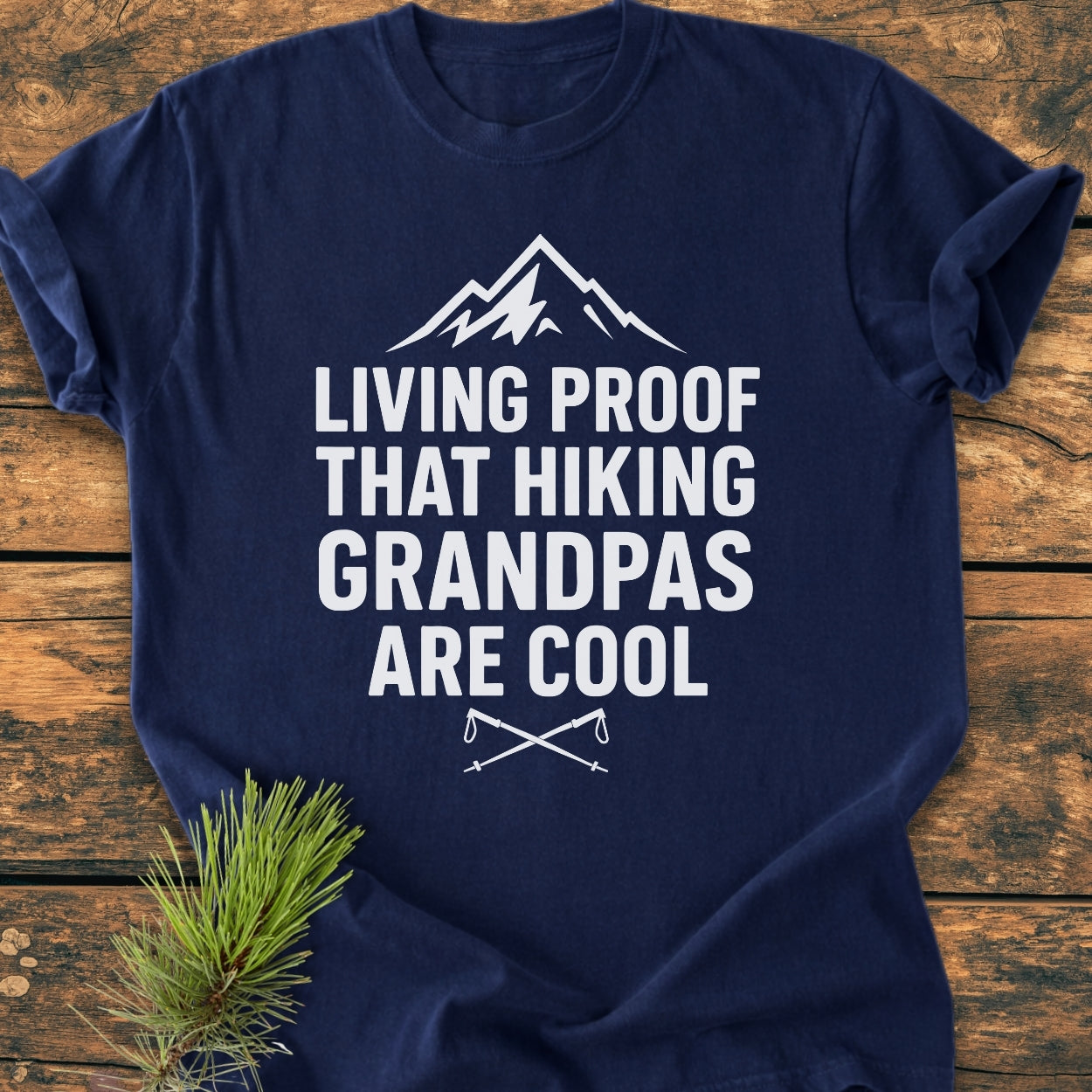 Living Proof Grandpa - Vintage Wash Tee featuring a mountain outline and trekking poles, displayed on a wooden surface with a pine branch accent. Soft, durable, relaxed fit for hiking enthusiasts.