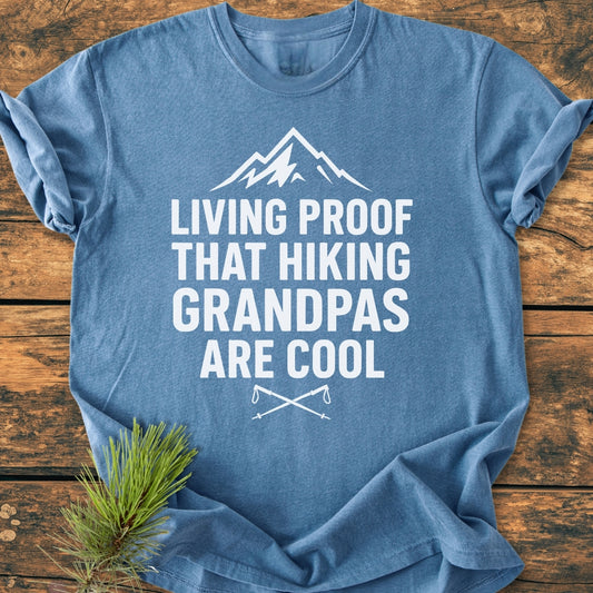 Living Proof Grandpa - Vintage Wash Tee featuring a mountain graphic, bold text celebrating hiking grandpas, and crossed hiking poles. Displayed on wood with a pine sprig for an outdoorsy vibe.