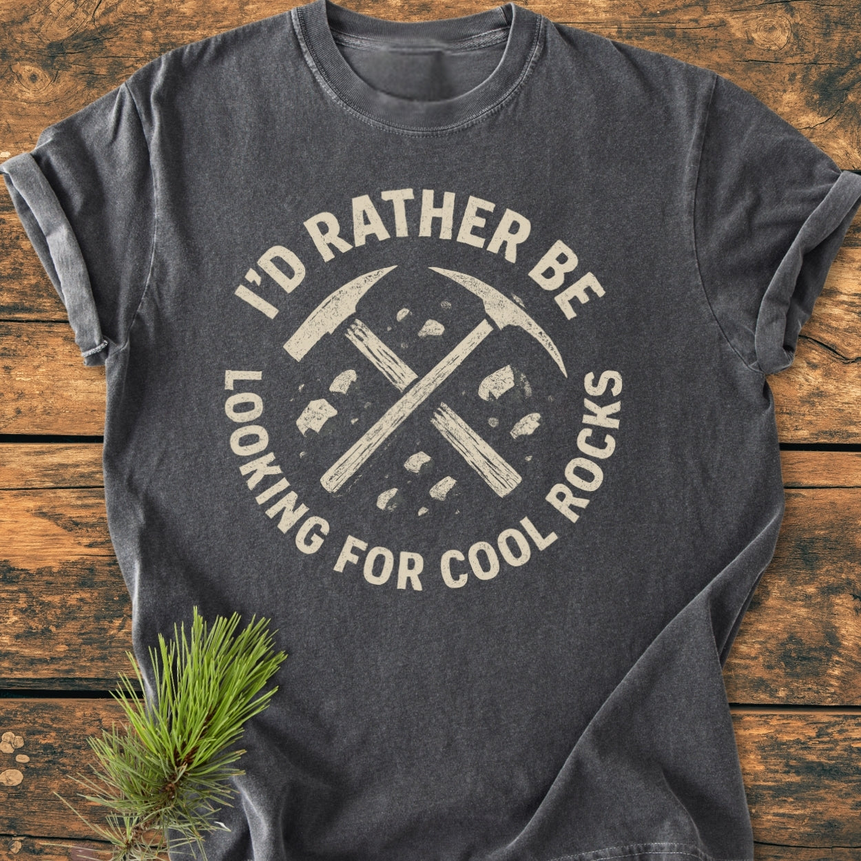 I'd Rather... Rockhound - Vintage Wash Tee featuring crossed pickaxes graphic, laid on wood, with durable, relaxed fit, 100% ring-spun cotton, for cozy, everyday wear. Pine sprig accents the scene.