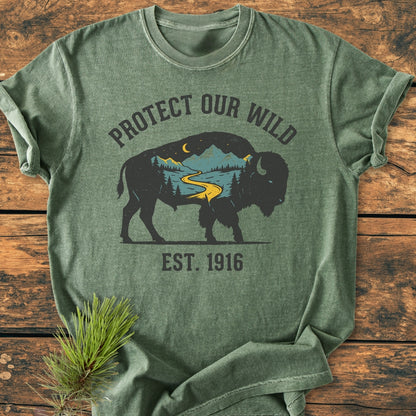 Protect Our Wild - Vintage Wash Tee featuring a buffalo graphic with a river, trees, and moon, laid on wood with a pine sprig, emphasizing its cozy, durable design.