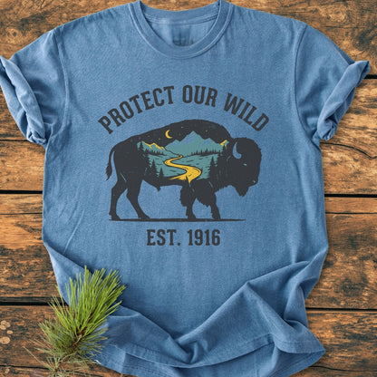 Protect Our Wild - Vintage Wash Tee features a bison graphic with a wilderness scene, including a river and mountains, on a heather-blue T-shirt, emphasizing outdoor protection.