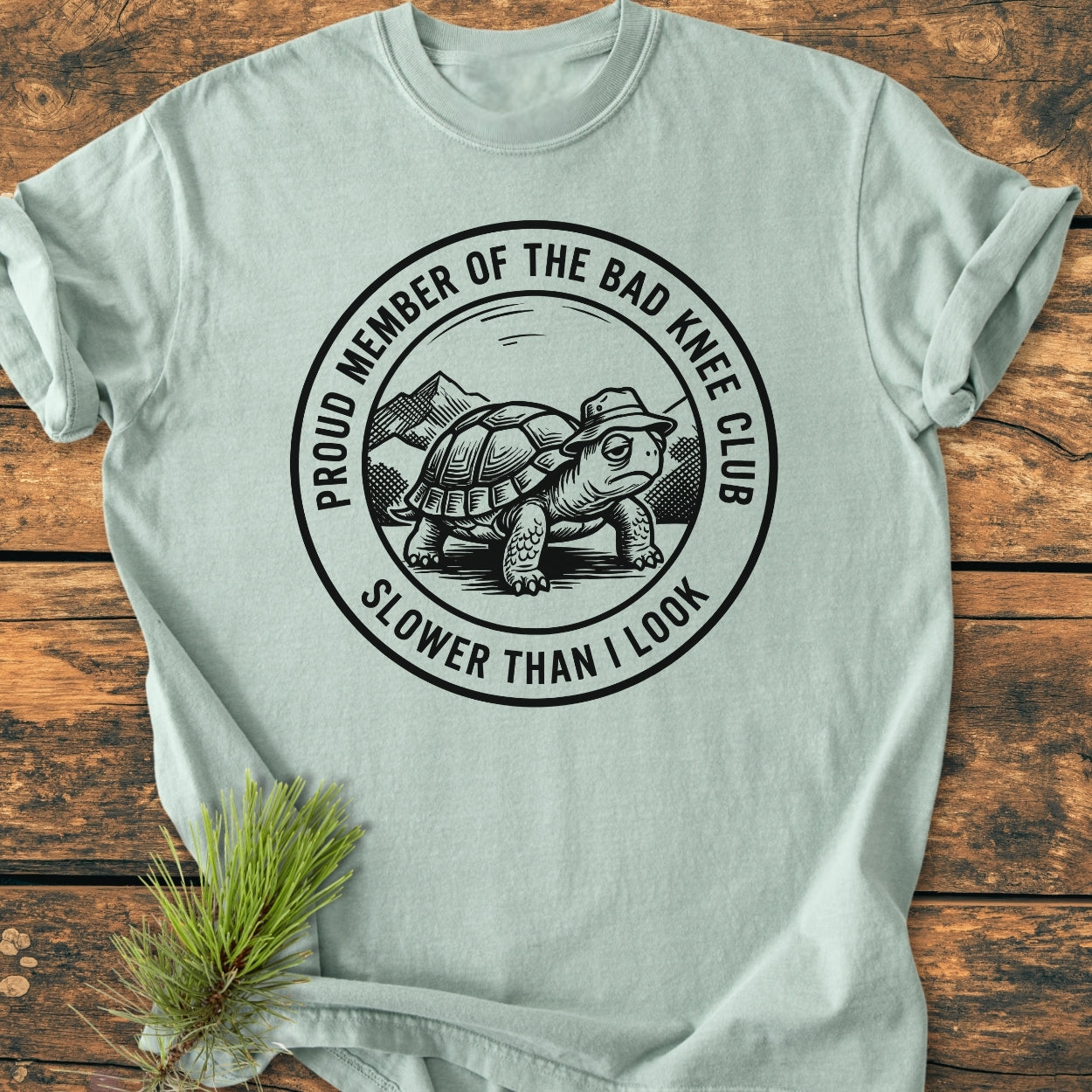 Bad Knee Club - Vintage Wash Tee features a cartoon tortoise illustration with text, PROUD MEMBER OF THE BAD KNEE CLUB and SLOWER THAN I LOOK, on a soft-washed, relaxed-fit T-shirt.