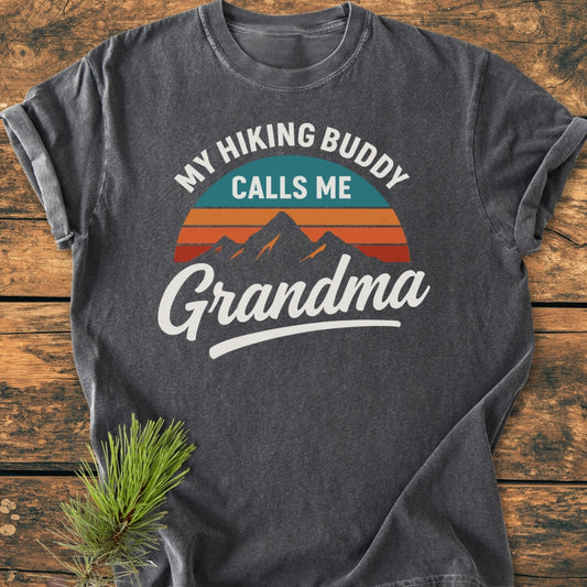 Hiking Buddy Grandma - Vintage Wash Tee in dark-heather gray, featuring a stylized sunrise mountain graphic. Laid on wood, it embodies comfort with a relaxed fit and durable, soft-washed cotton.