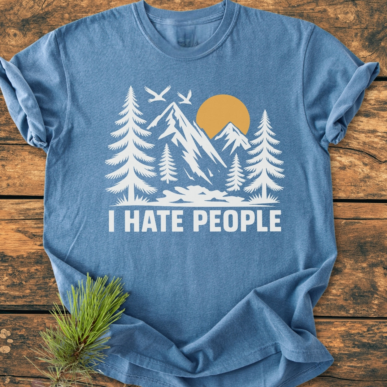 I Hate People - Vintage Wash Tee: Blue crew-neck T-shirt featuring a white and gold nature scene with mountains, sun, trees, and birds, complemented by bold lettering. Soft, durable, and pre-shrunk cotton.