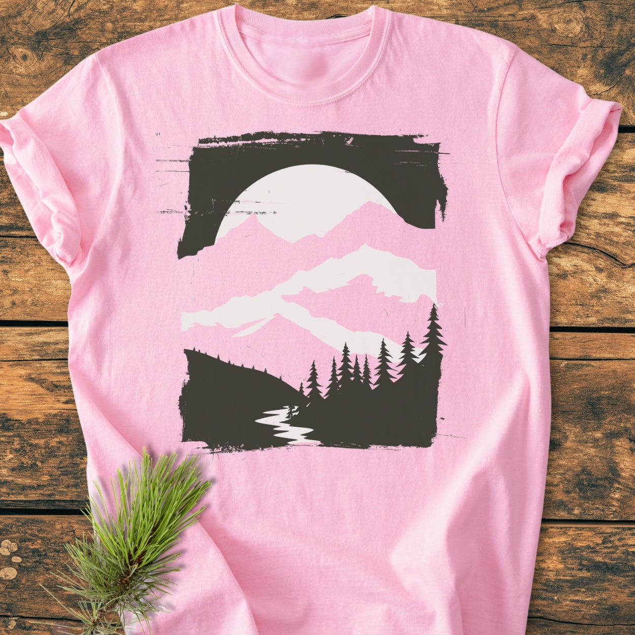 Minimalist Mountains - Vintage Wash Tee featuring a nature scene with mountains, trees, and a river. Laid flat, showcasing its relaxed fit and durable double-needle stitching, alongside a pine sprig.