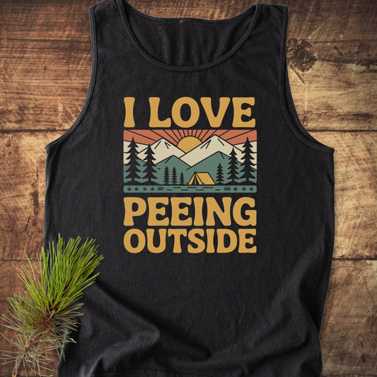 Black I Love Peeing Outside Tank Top featuring a mountain camping scene with pine trees, a tent, and a rising sun, styled with a pine branch on a wooden surface.