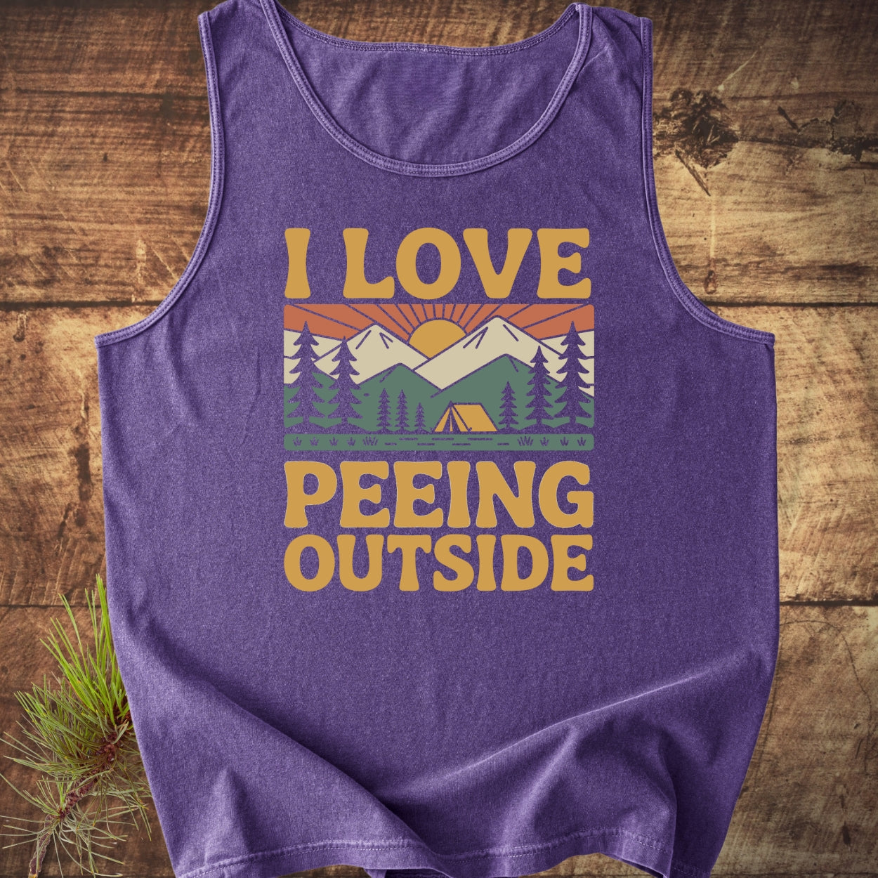 I Love Peeing Outside Tank Top features a retro mountain scene with mustard text on a purple sleeveless shirt, crafted from 100% ring-spun US cotton for sustainable, relaxed wear.