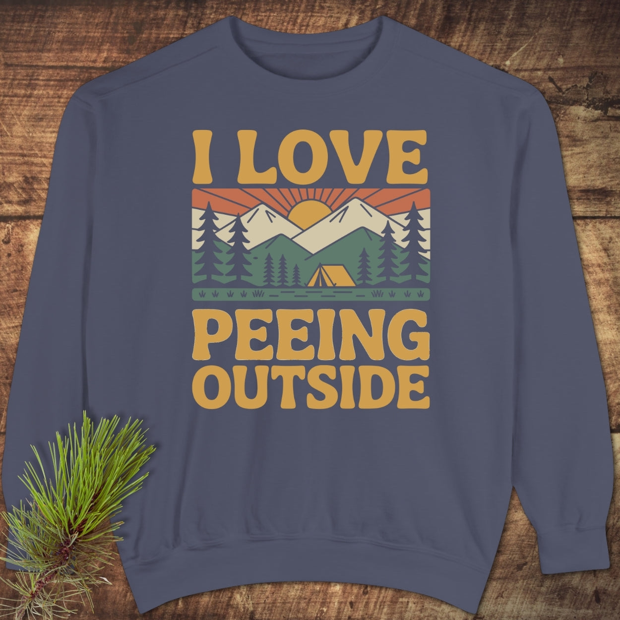 The I Love Peeing Outside Sweatshirt features a retro camping scene with a sunrise, mountains, trees, and a tent, highlighted by a bold slogan on a navy-blue crewneck sweatshirt.