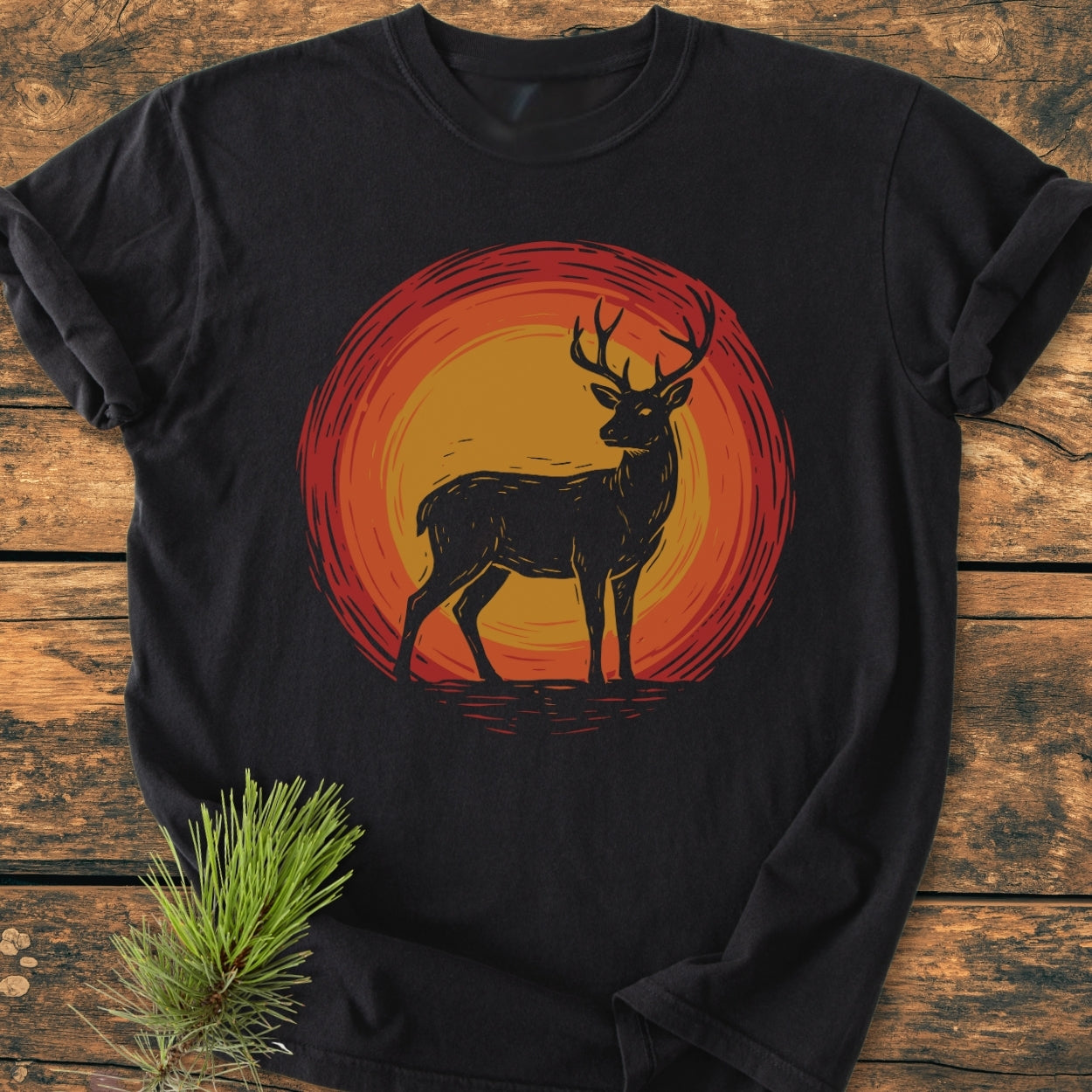 Trail Guardian - Vintage Wash Tee features a black T-shirt with a silhouetted deer graphic against a sunset motif, displayed on wood, highlighting its soft, relaxed fit and garment-dyed cotton texture.