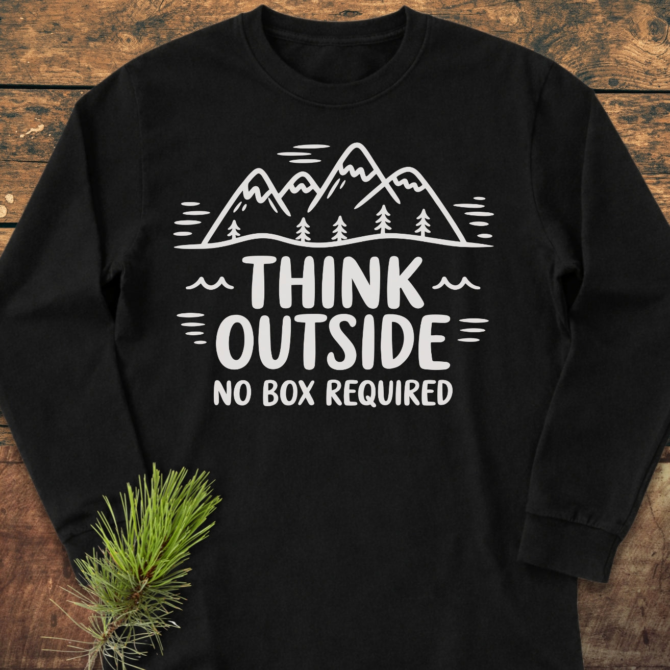 Think Outside Long-Sleeve Tee features a stylized mountain and tree line with the phrase THINK OUTSIDE NO BOX REQUIRED. Laid flat, emphasizing its relaxed fit and soft, garment-dyed cotton fabric.
