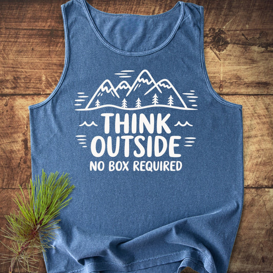 Think Outside Tank Top featuring a mountain-and-tree graphic with THINK OUTSIDE slogan, laid flat on wood. Beside it, a pine branch complements the garment's nature-inspired theme.