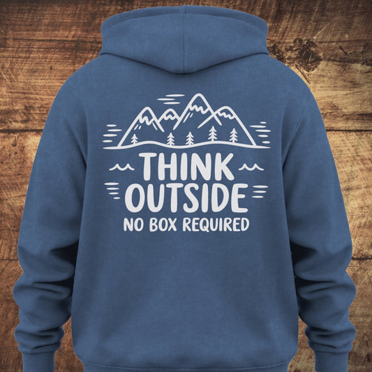 Think Outside Hoodie BACKPRINT featuring a mountain and tree line-drawing with THINK OUTSIDE NO BOX REQUIRED slogan, displayed on a wooden backdrop, showcasing its relaxed fit and trail-inspired design.