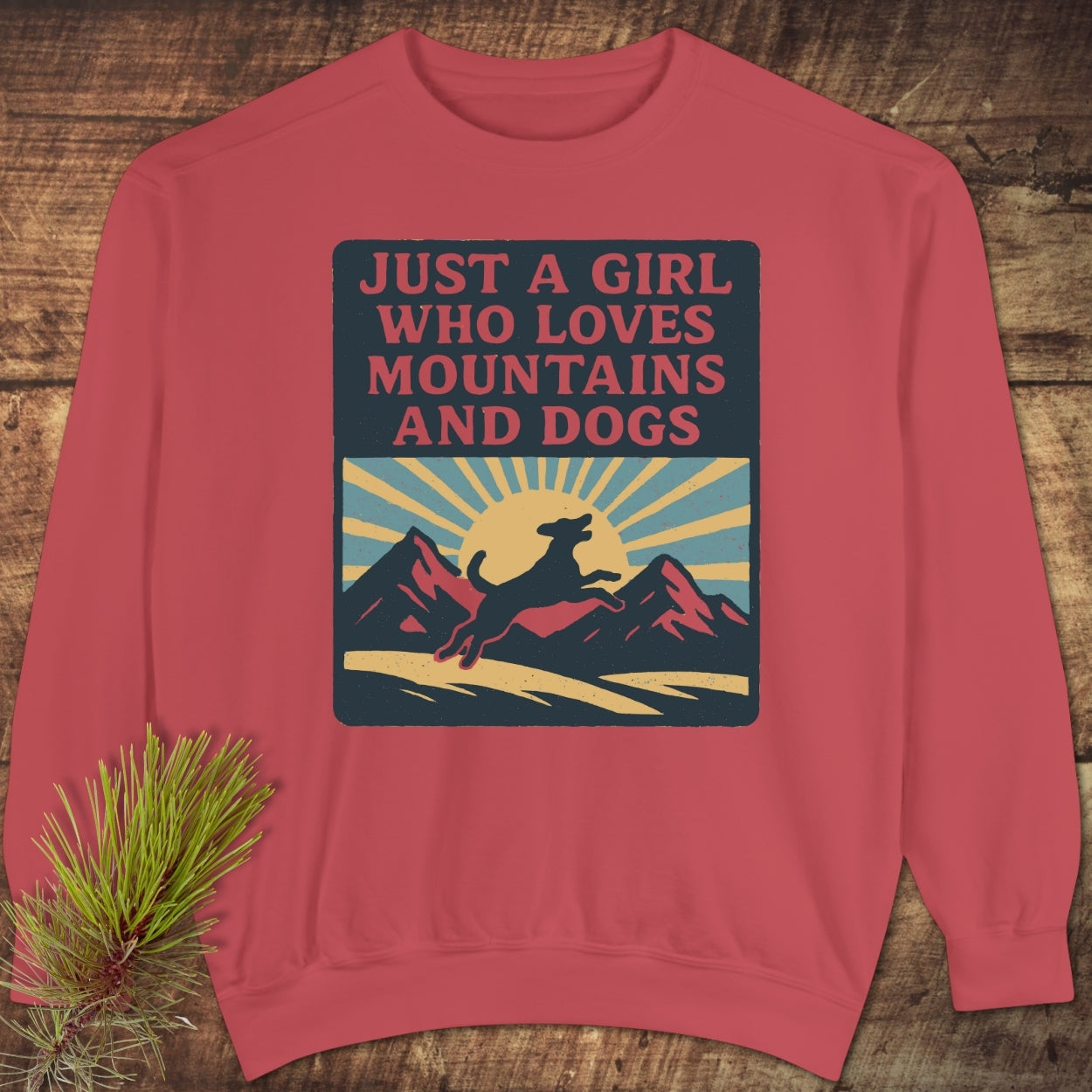 Just A Girl Who Loves Dogs Sweatshirt displayed on wood, featuring a graphic of a dog, sunrise, and mountains. Highlights relaxed fit with ring-spun cotton blend for luxurious comfort and style.