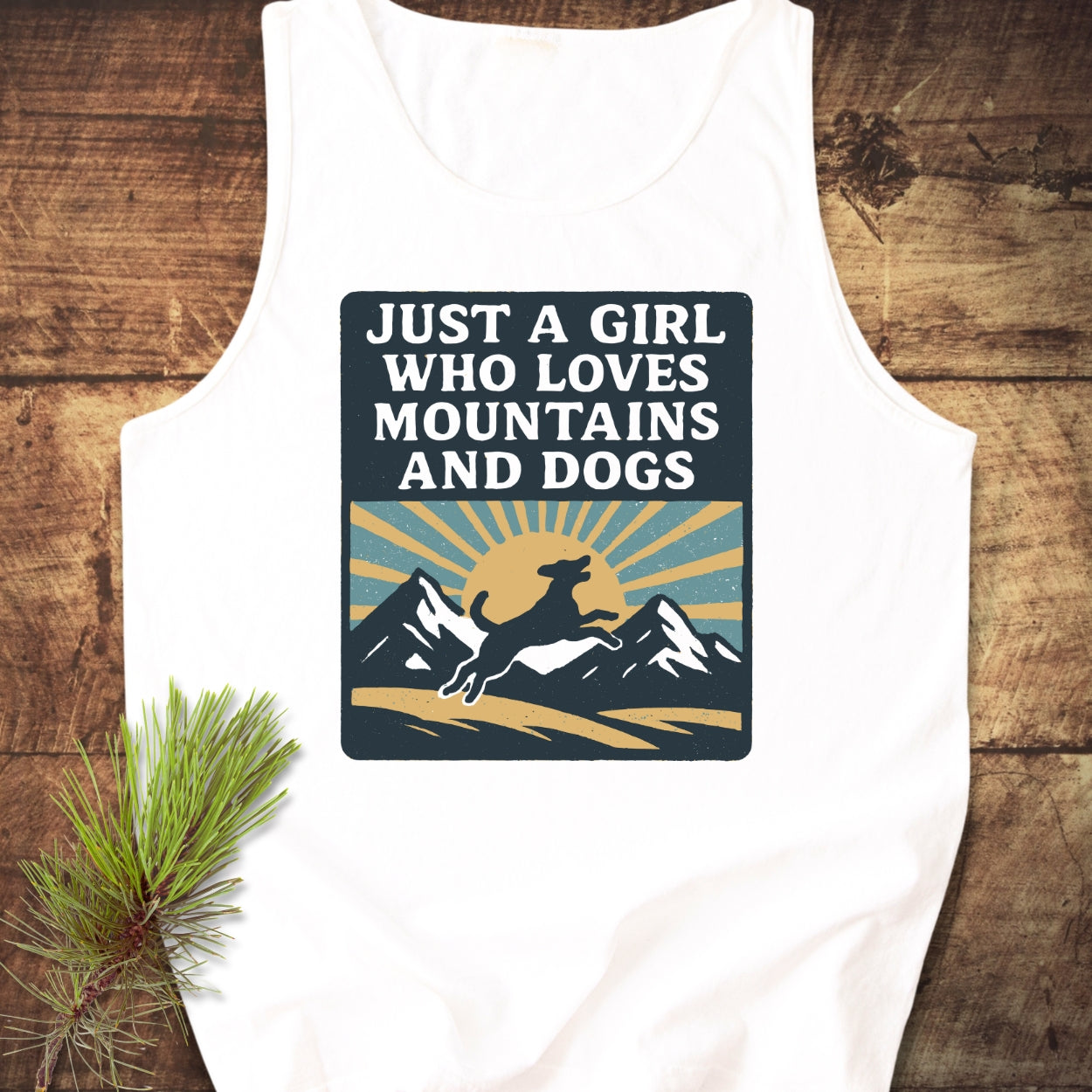 Just A Girl Who Loves Dogs Tank Top featuring a retro-style graphic of a sun, mountains, and a leaping dog, laid on wood, highlighting its relaxed fit and sustainable design.