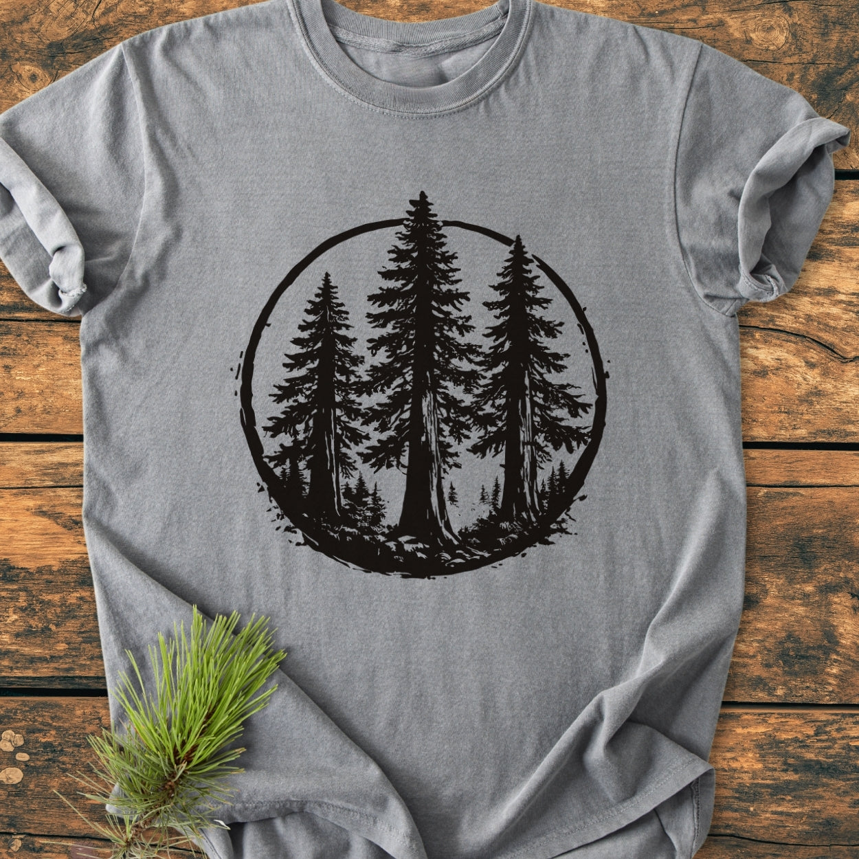 Redwood Trees - Vintage Wash Tee laid flat, featuring a black graphic of tall evergreens. Made of soft, garment-dyed 100% ring-spun cotton, designed for comfort and durability. Includes a fresh pine branch accent.