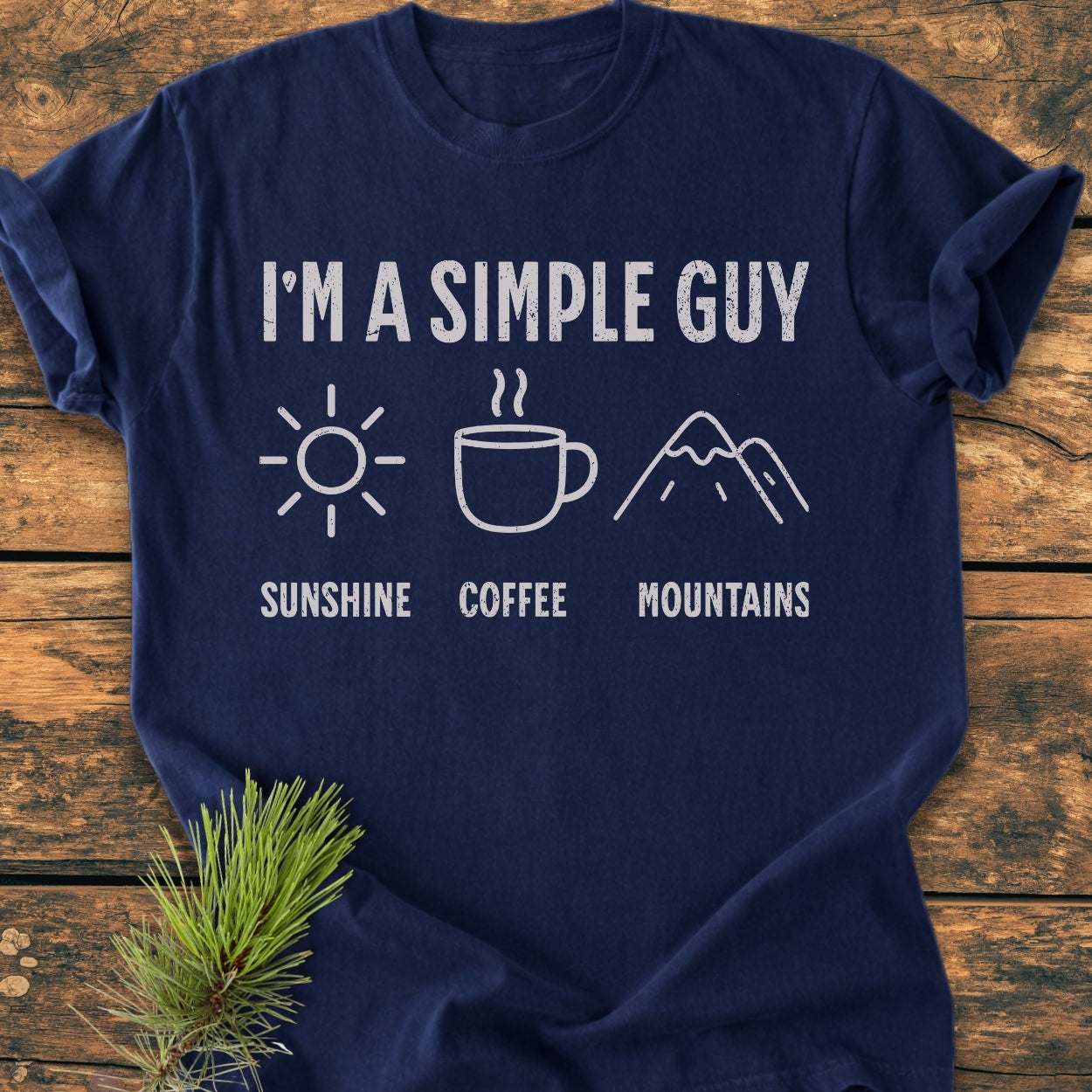 I'm A Simple Guy - Sunshine Coffee Mountains - Vintage Wash Tee displayed on wood, featuring distressed white text and icons of a sun, coffee mug, and mountains; crafted from garment-dyed, 100% ring-spun cotton.