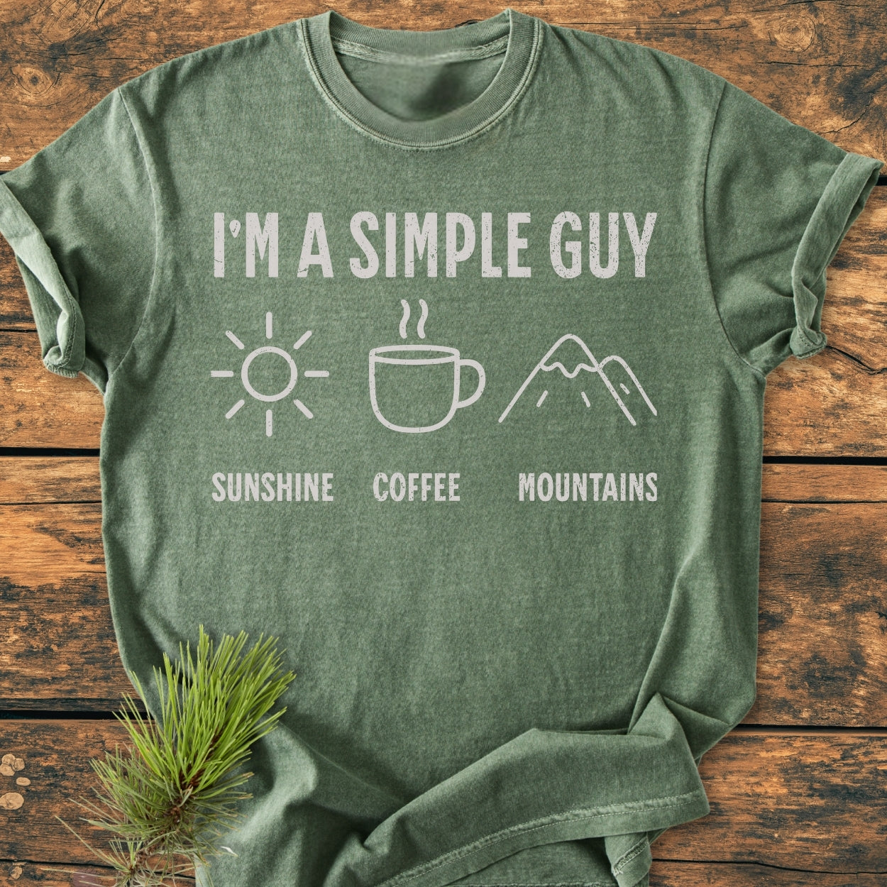 I'm A Simple Guy - Sunshine Coffee Mountains - Vintage Wash Tee displayed on wood, featuring white text and icons of a sun, coffee cup, and mountains, highlighting its casual and comfortable fit.