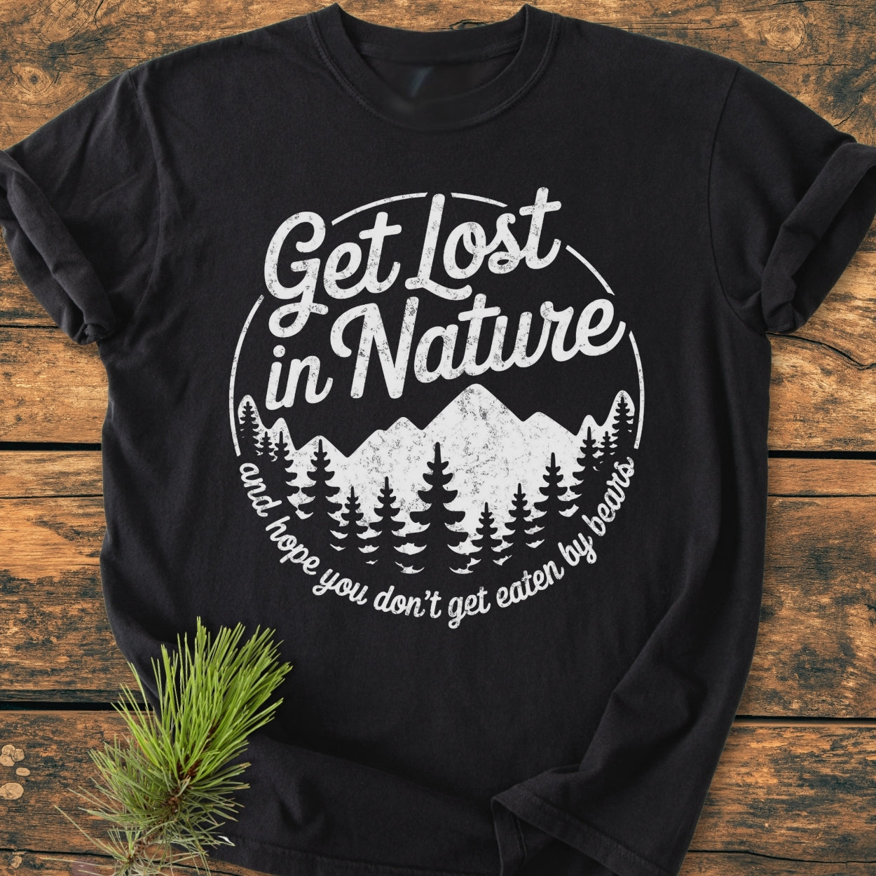 Get Lost In Nature - Vintage Wash Tee features a distressed mountain and tree graphic with playful text on a black, soft-washed, garment-dyed T-shirt, enhanced by a pine sprig accent.