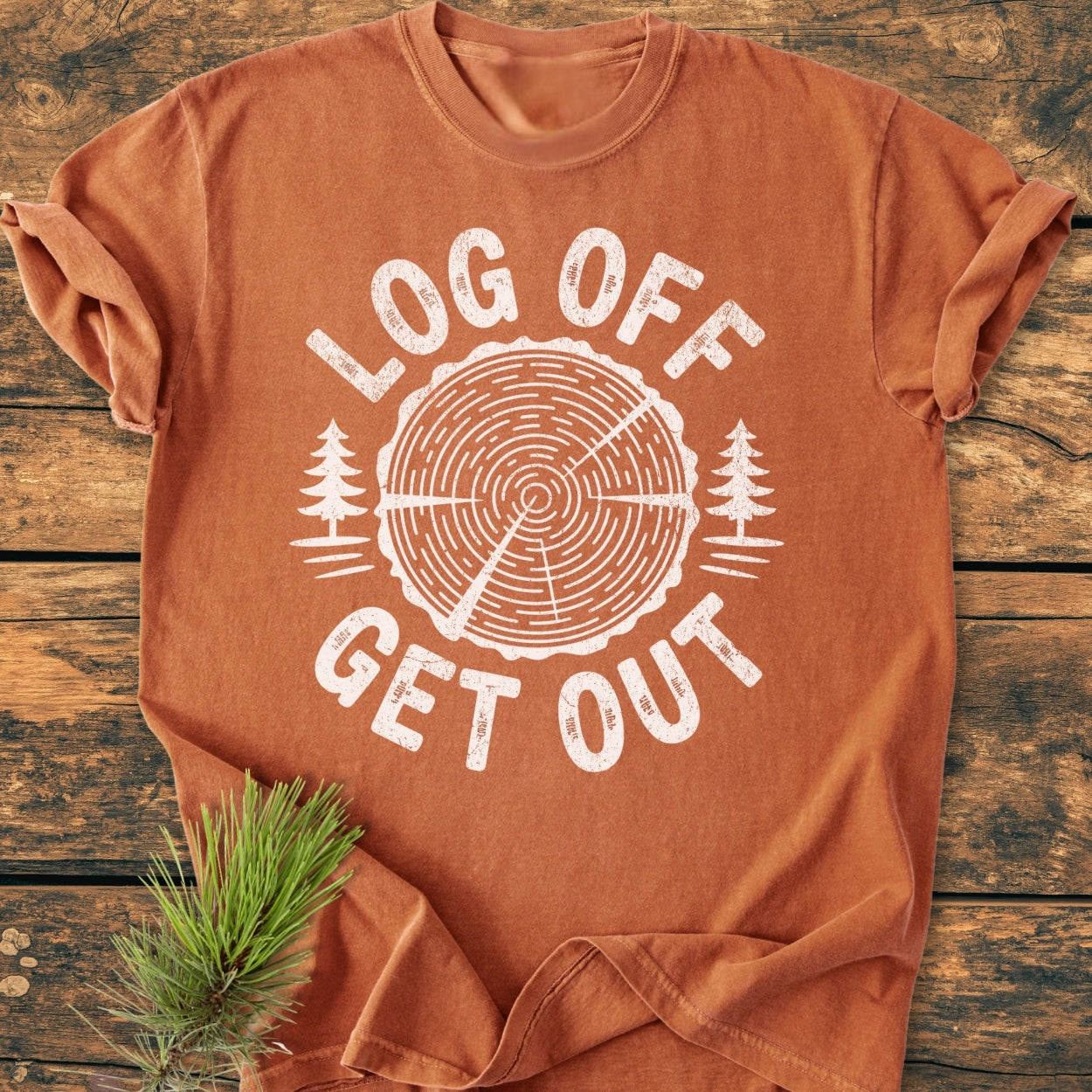 Log Off Get Out - Vintage Wash Tee features a tree trunk design with LOG OFF and GET OUT text, laid on a wooden surface, emphasizing its relaxed fit and durable, soft-washed fabric.